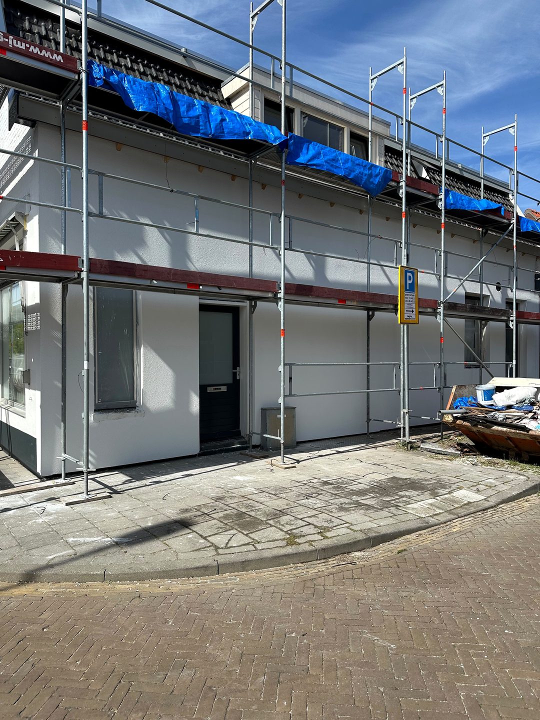 Wit gestucte gevel van een rijwoning, met de steiger nog aan de gevel
